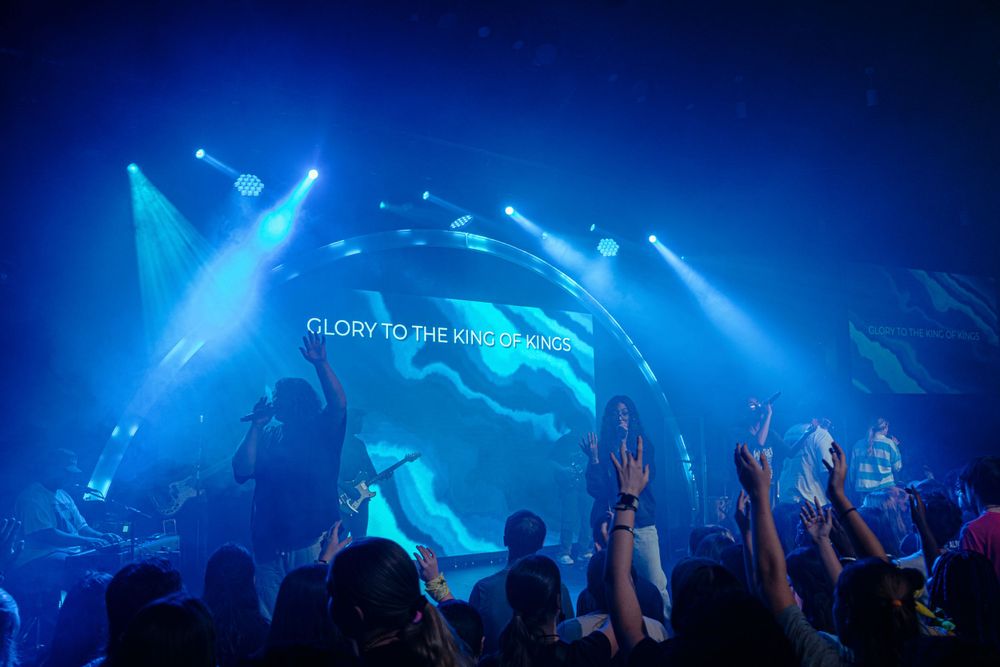 Concert crowd raises hands as blue stage lights illuminate Glory to the King worship event.
