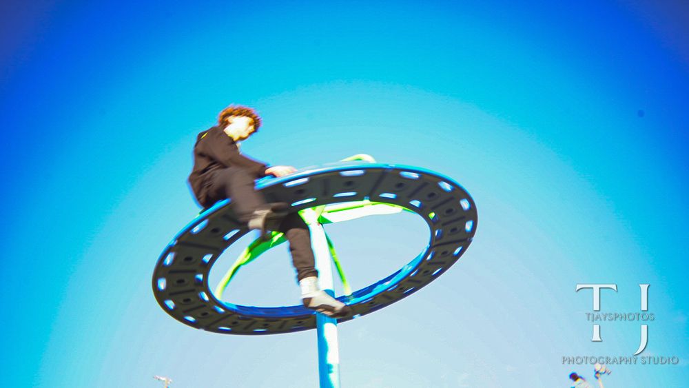 Performer balances on large spinning hoop high above stage against blue background.