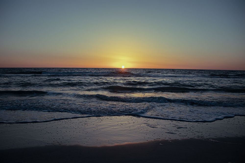 Serene ocean sunset with gentle waves washing onto a sandy beach under a clear sky.