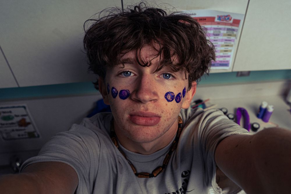Teen takes selfie with purple circle stickers on face in a colorful room.