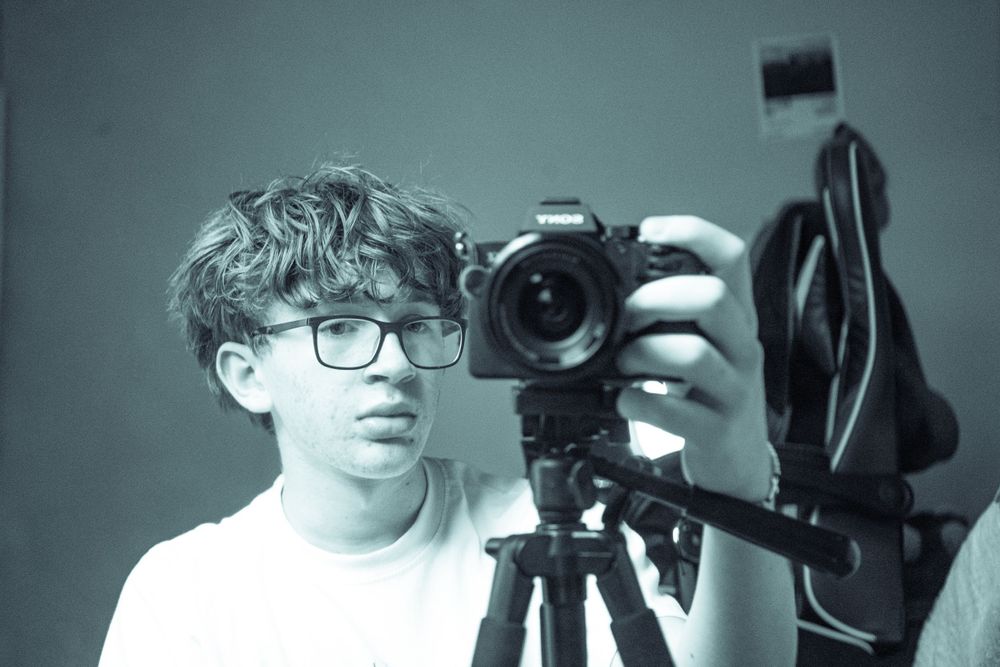 Young photographer adjusts DSLR camera on tripod in black and white portrait.