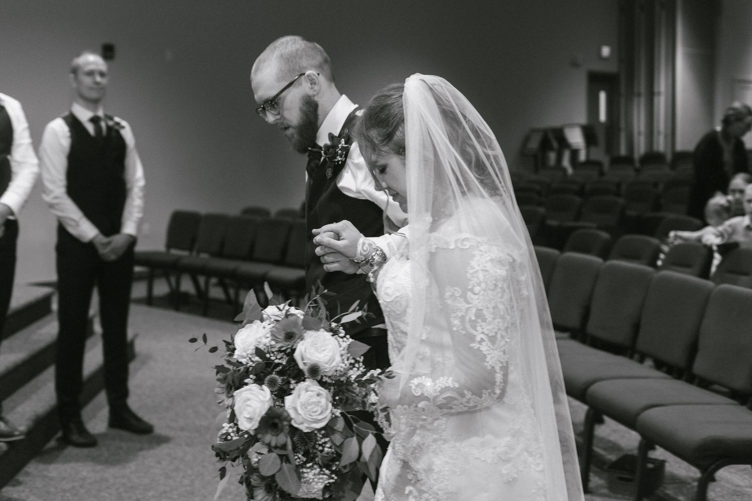 Wedding party gathers on a modern rustic stage with wooden pallet backdrop in a church sanctuary setting.