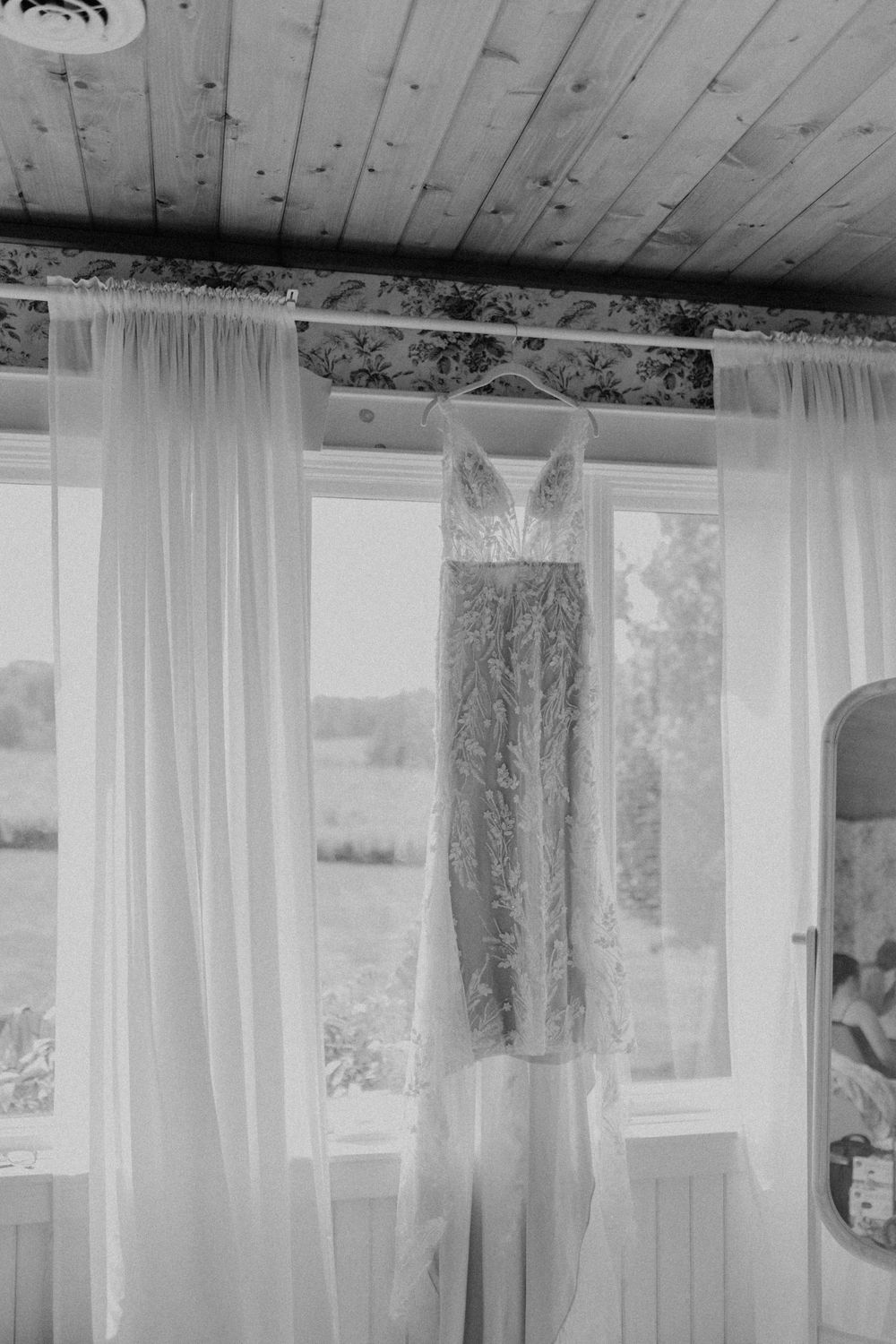 Elegant lace wedding dress hanging in a window in black and white photography.