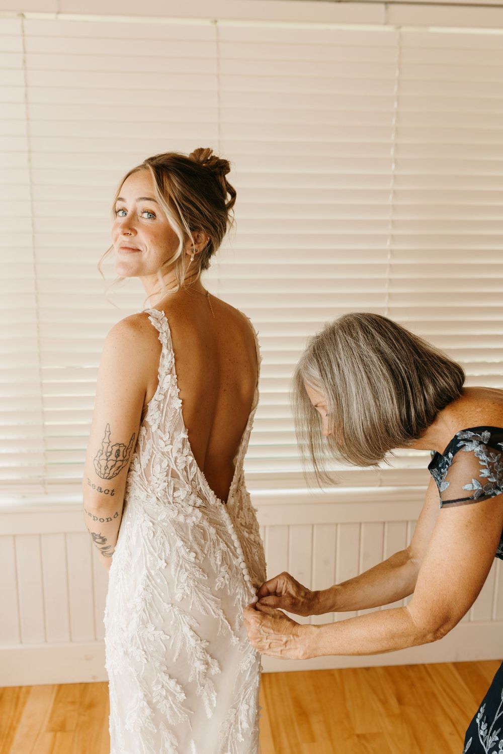 Mother helping bride into a backless lace wedding dress before the ceremony.