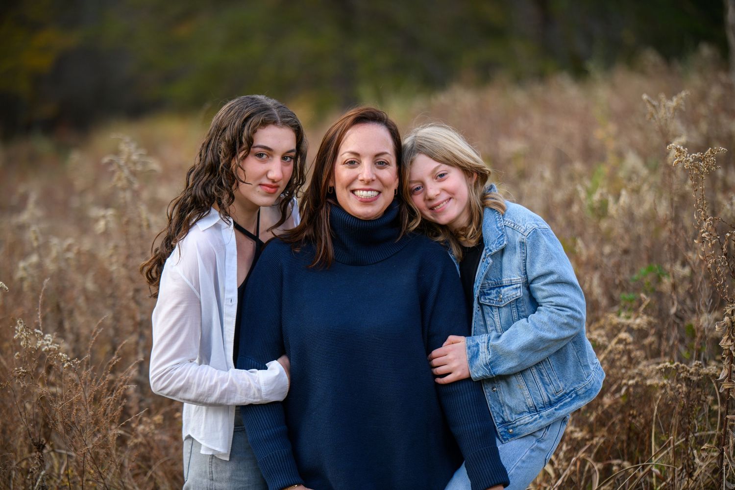 Three people embrace while posing together in a field of tall autumn grass.
