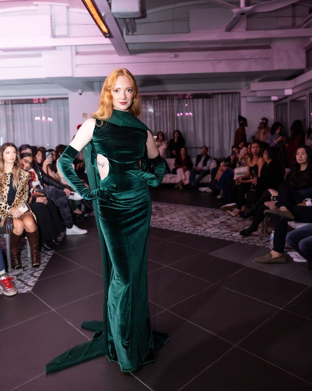 Model poses in elegant emerald velvet evening gown during indoor fashion show.