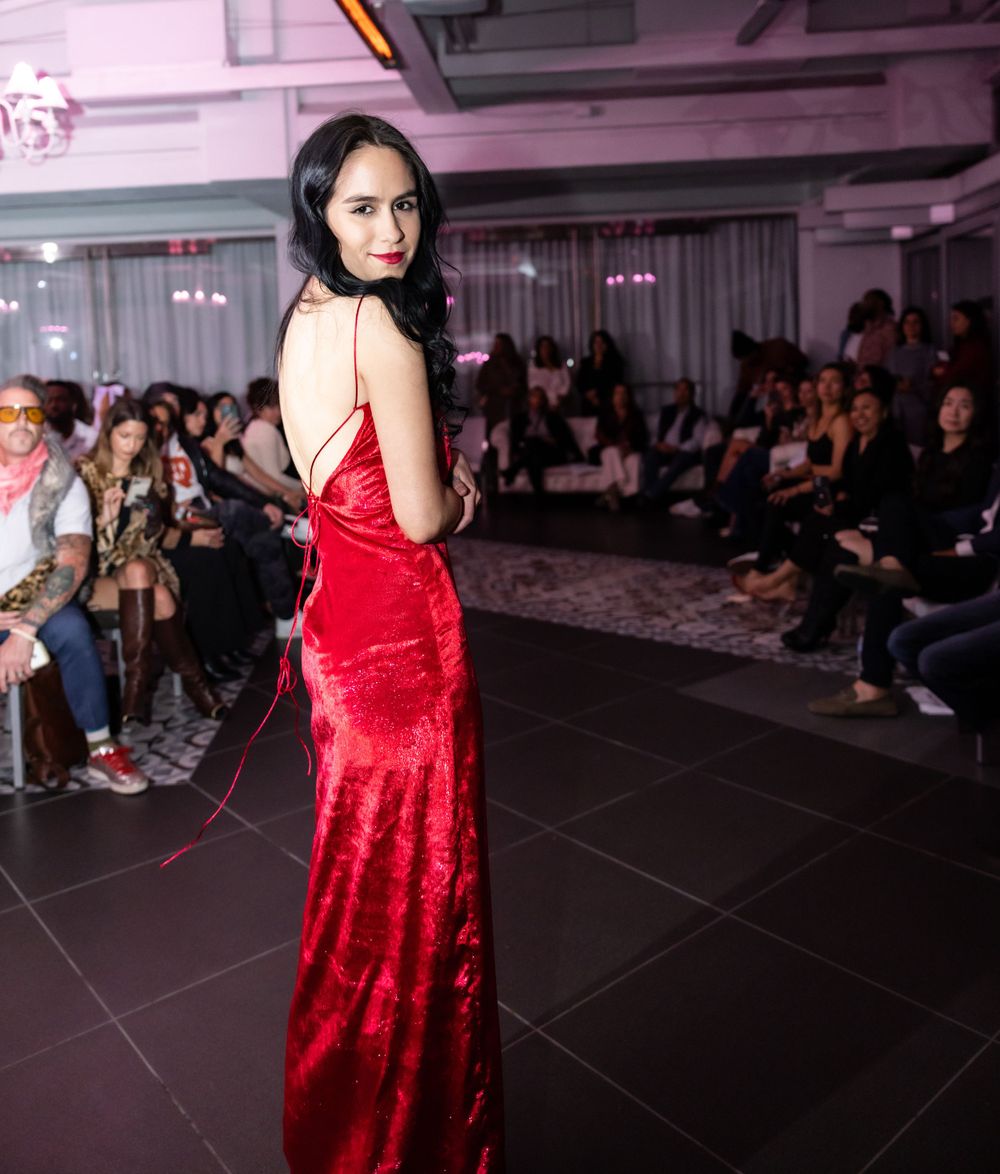 Model in red satin evening gown poses on runway with dramatic back detail.