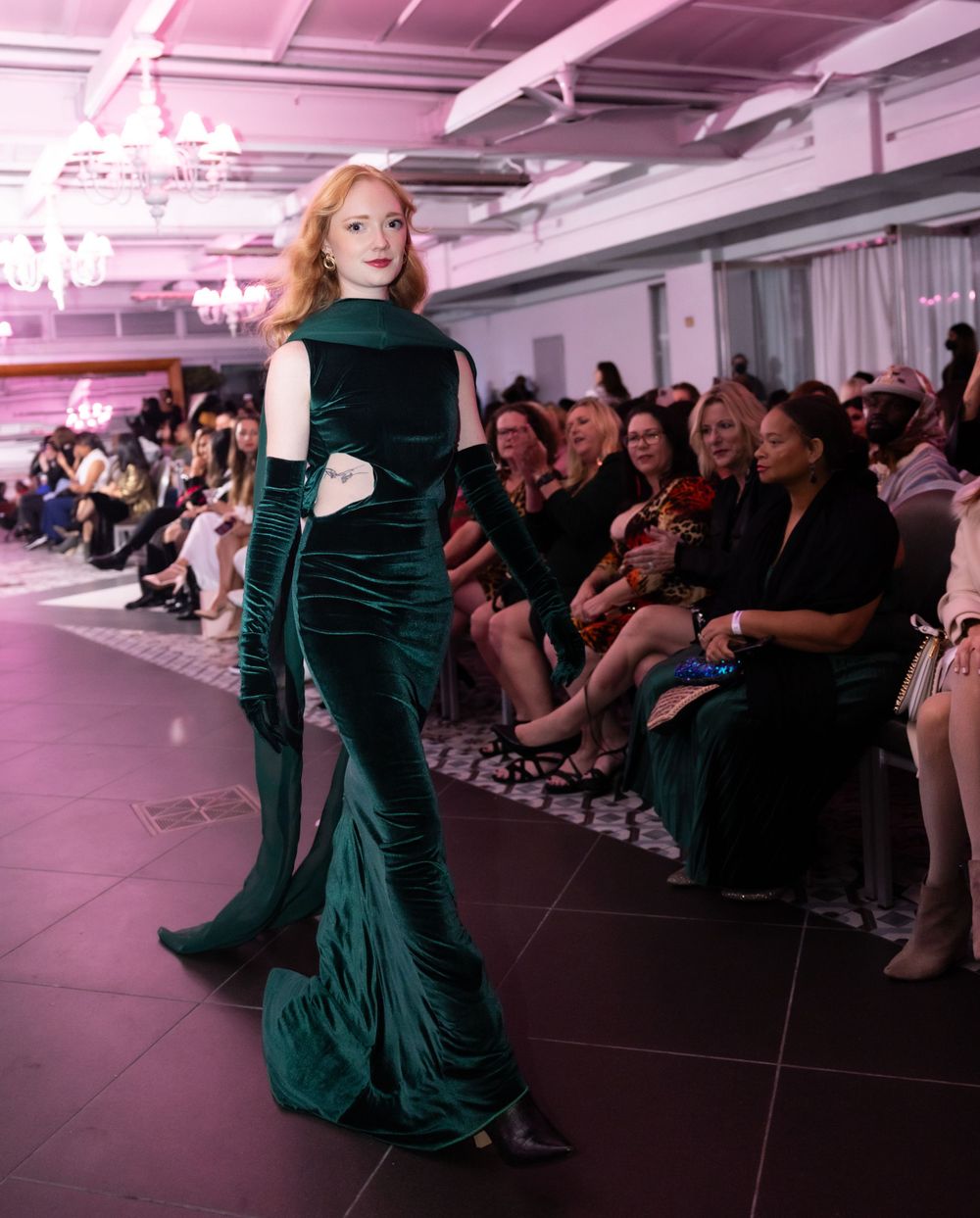 Emerald green velvet gown with long gloves featured on illuminated fashion runway.