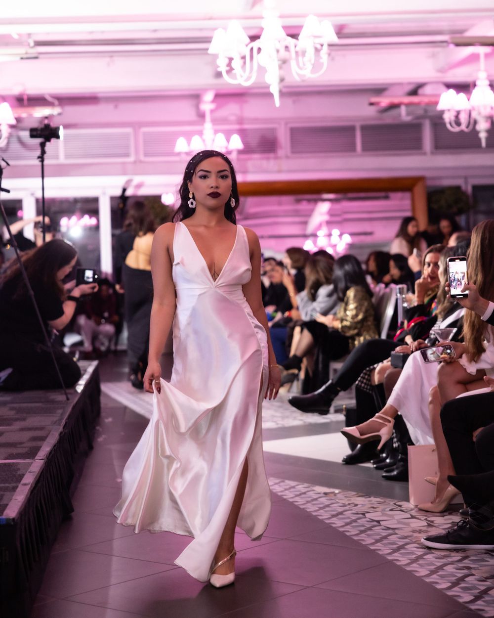Flowing white satin evening gown with plunging neckline displayed on pink-lit runway.