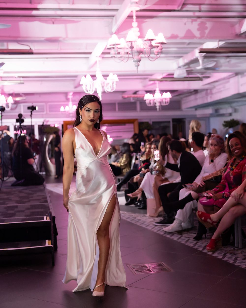 Elegant white silk gown with thigh-high slit showcased under pink chandeliers.
