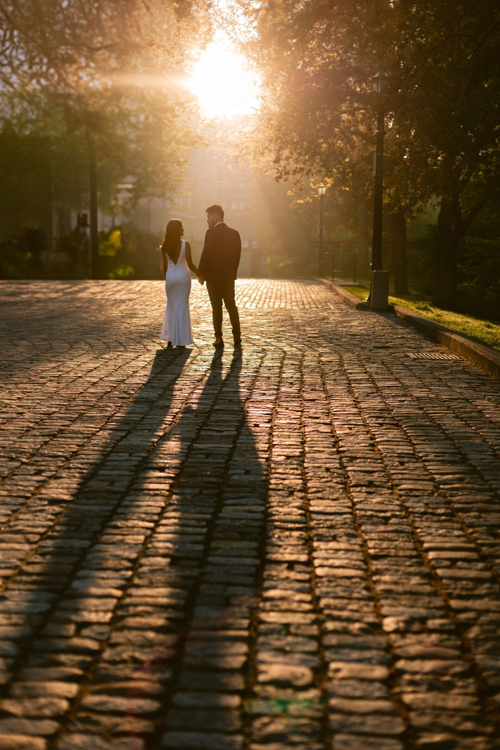 Silhouettes of a couple walking on cobblestone path at sunset with long shadows cast behind them.