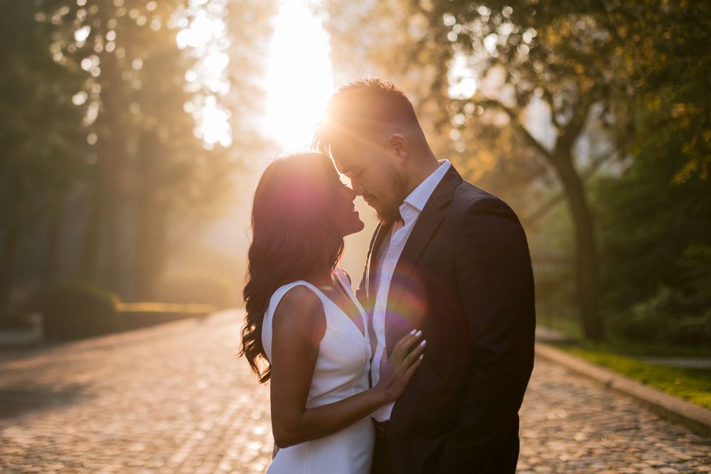 Romantic couple embracing on cobblestone path during golden hour with sunlight streaming through trees.
