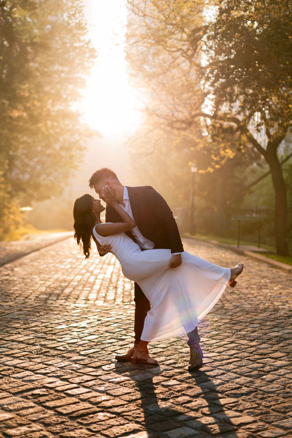 Couple in formal attire dancing on cobblestone street during sunset with dramatic dip pose.