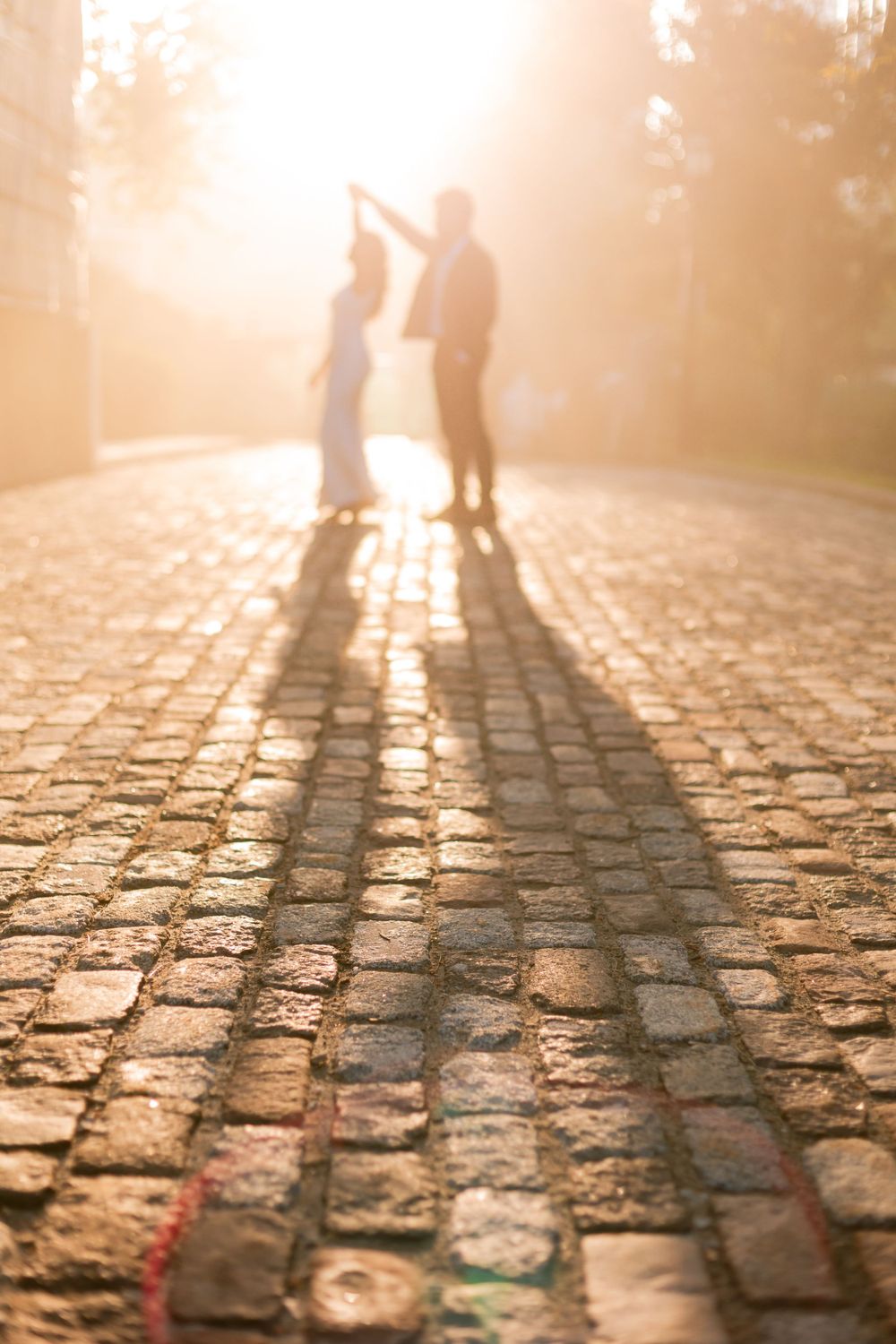 Silhouettes dancing on sunlit cobblestone street with long shadows stretching across the stones.