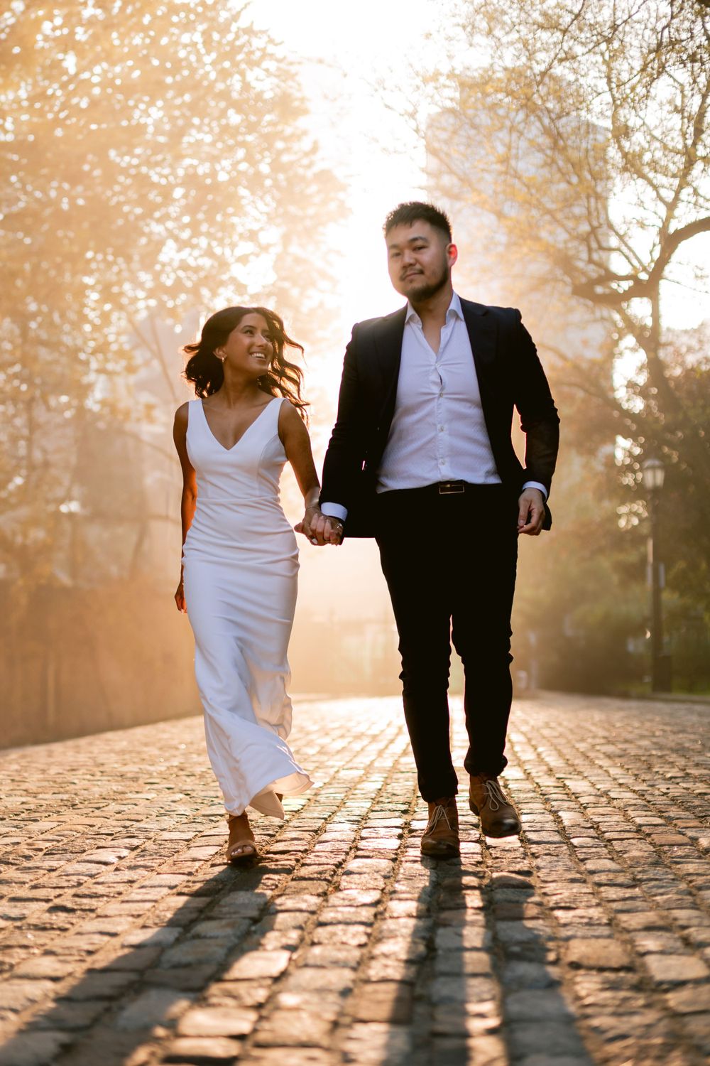 Couple walking hand in hand on cobblestone path during golden hour sunset.