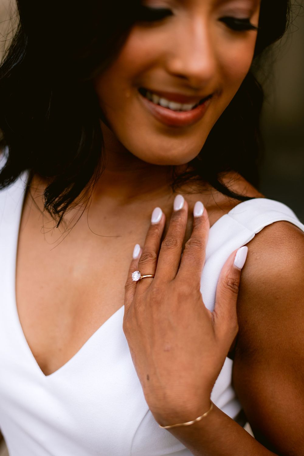 Close up of elegant engagement ring on hand with white dress and delicate bracelet.