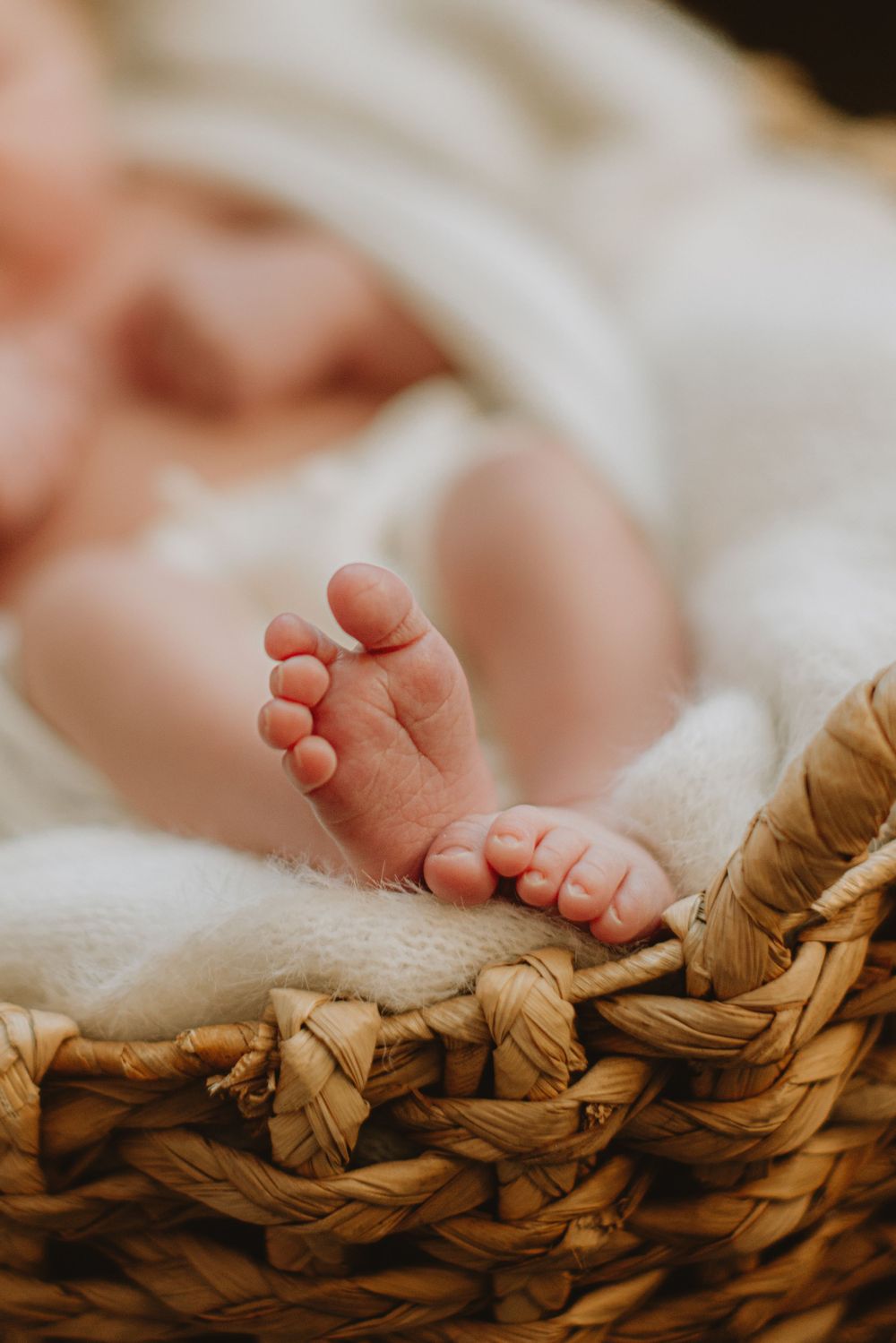 Tiny newborn baby feet resting on woven basket texture.