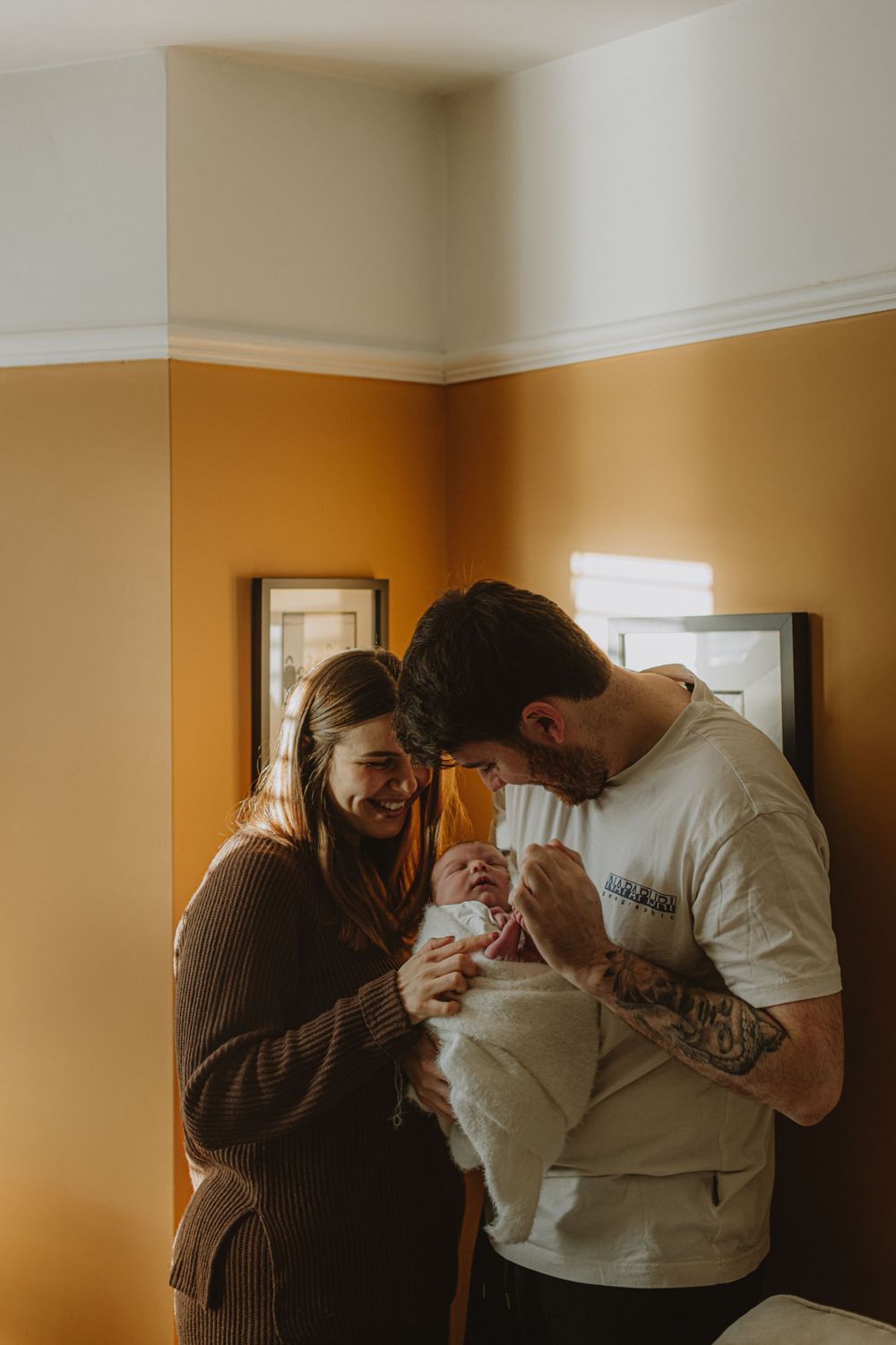 Couple sharing intimate moment while looking down at something together against orange wall.