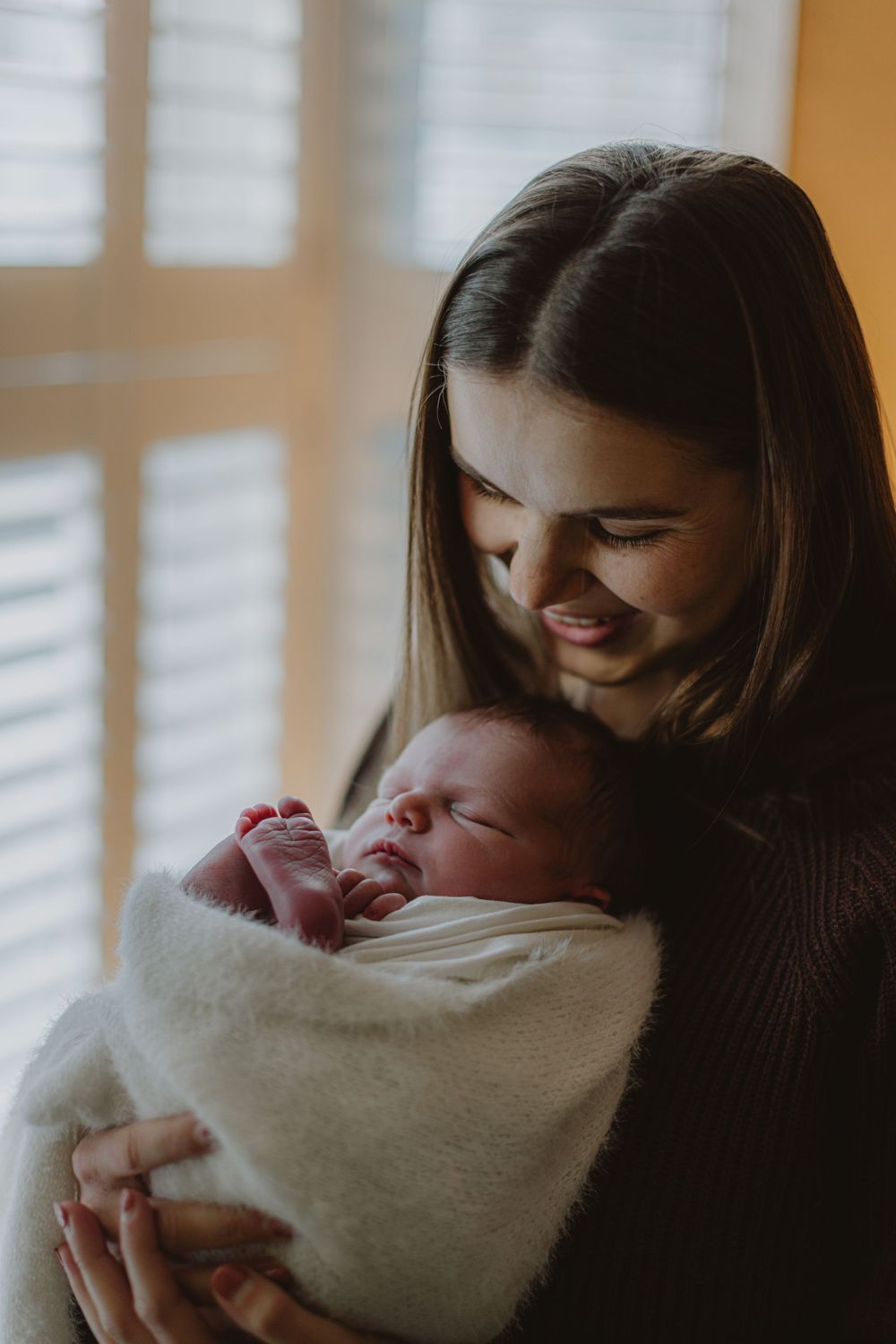 Parents gazing lovingly at their newborn baby wrapped in white blanket.