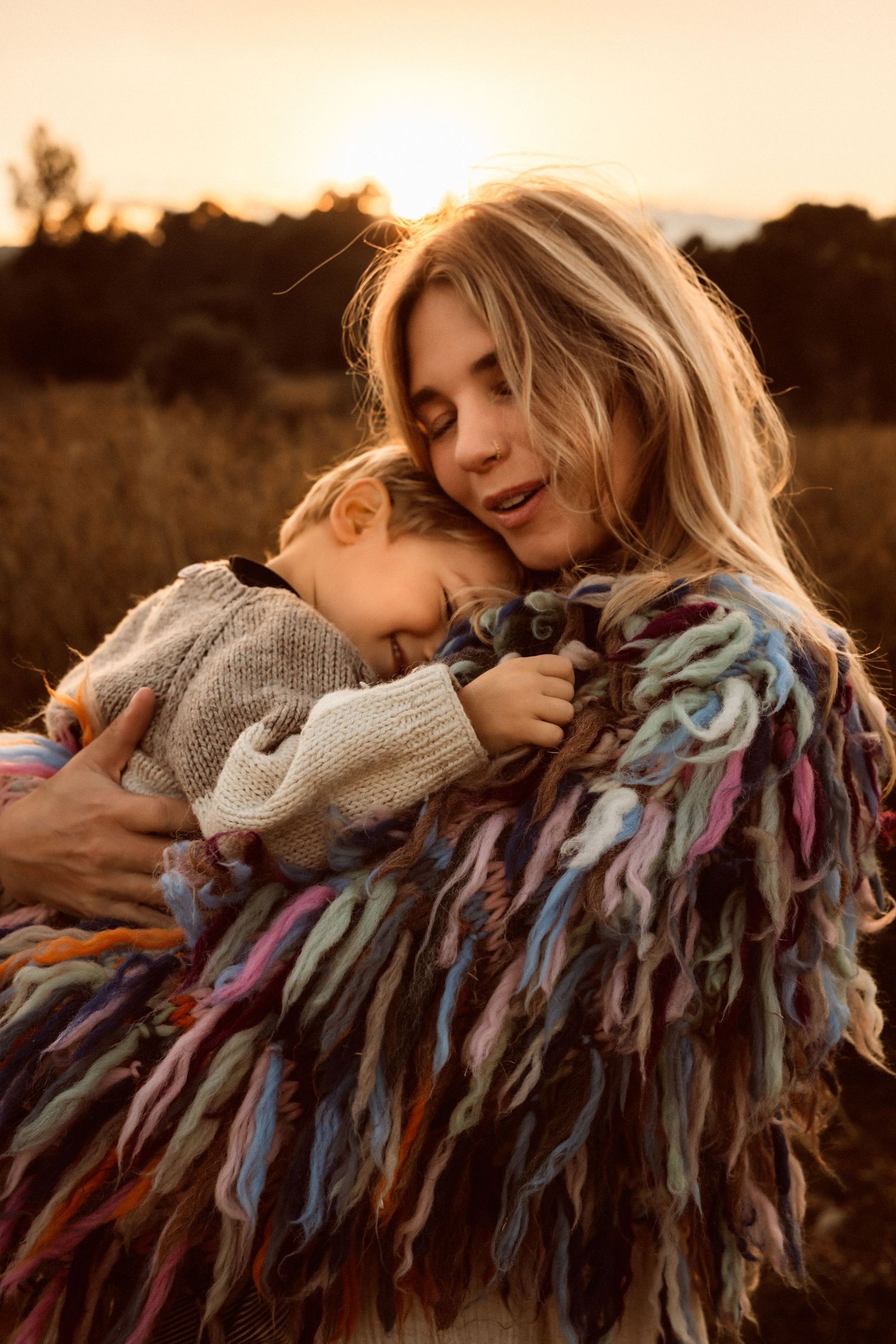 A mom and child share a tender embrace outdoors at sunset in Denia  while wearing cozy sweaters and colorful shawls. Denia photographer