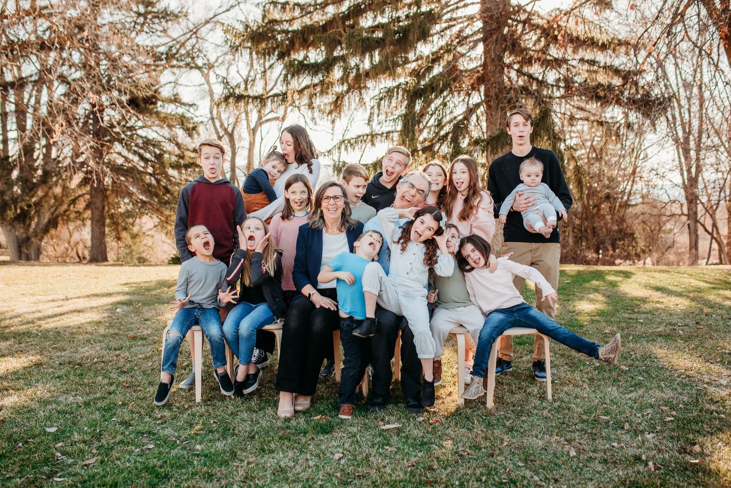 A cheerful multi-generational family group poses informally together under a large evergreen tree.