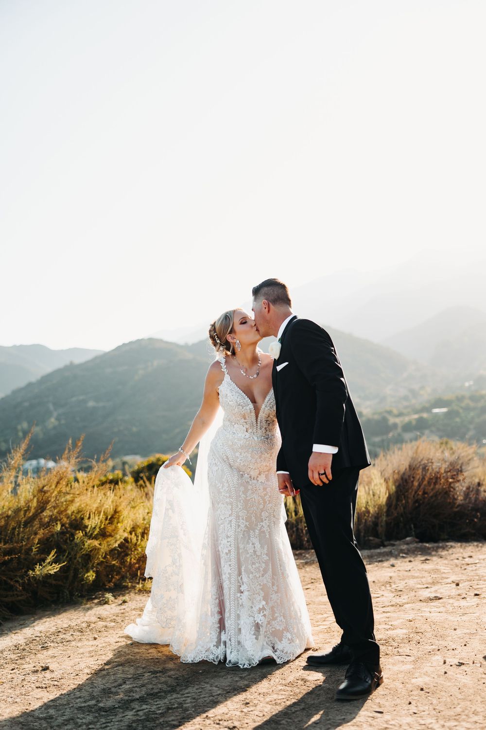 Romantic wedding couple share intimate moments against mountainous backdrop during golden hour photoshoot.