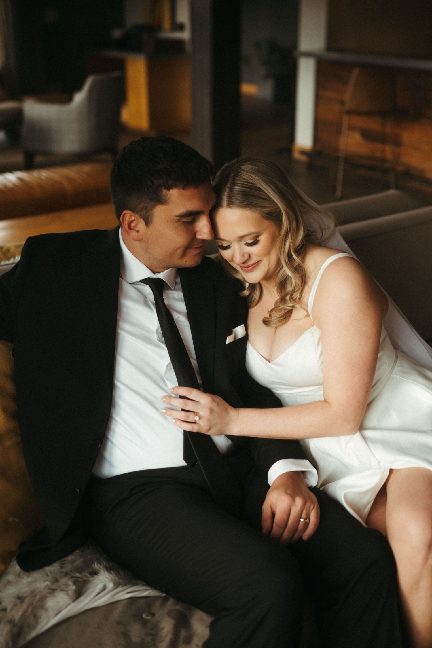 Intimate indoor wedding portrait of couple sharing tender moment on leather couch.