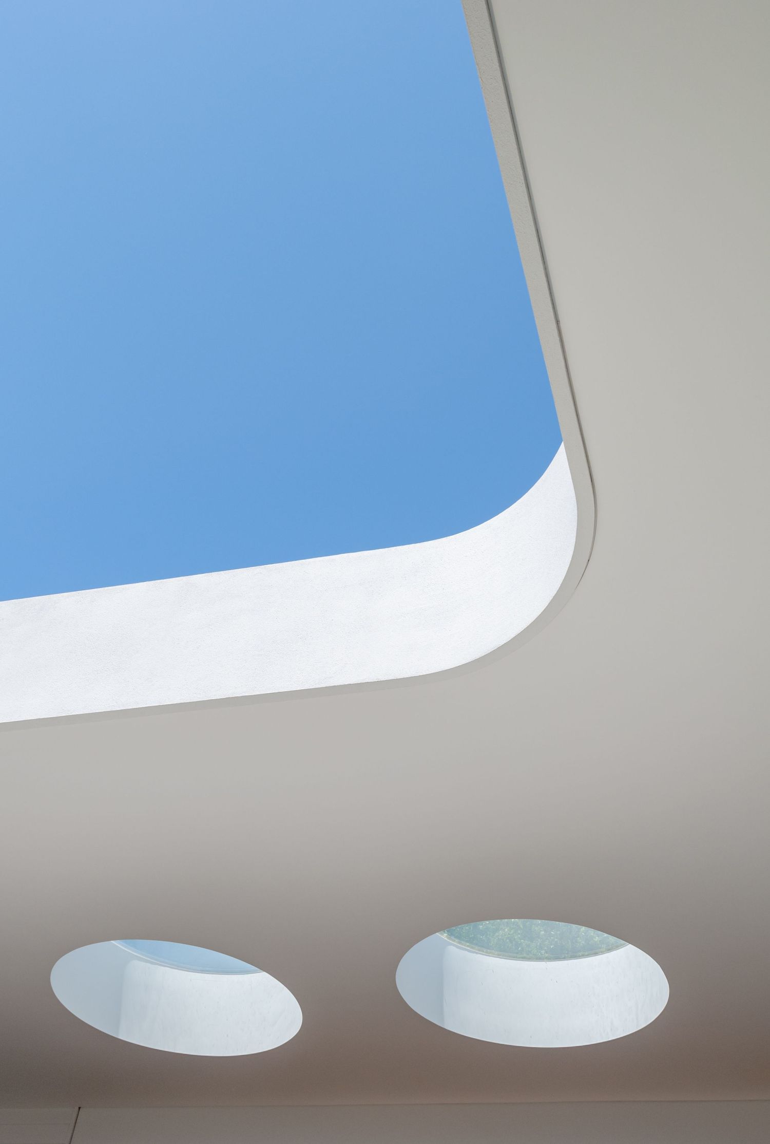 Minimalist architectural detail showing curved skylight windows against a bright blue sky.