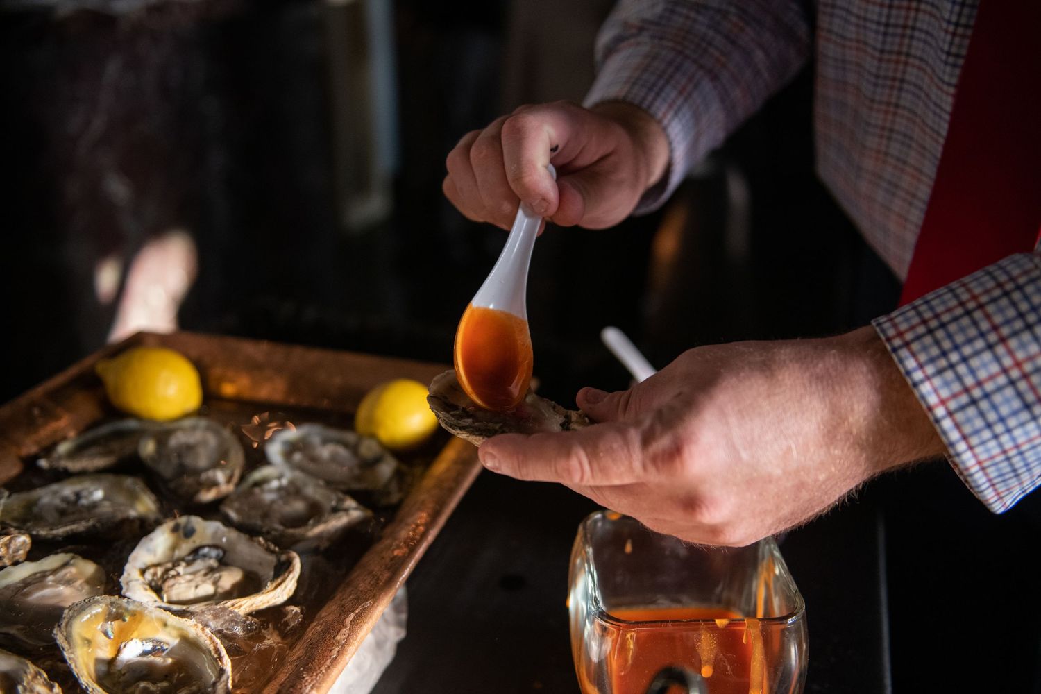 Hands shucking fresh oysters with lemons on wooden cutting board.