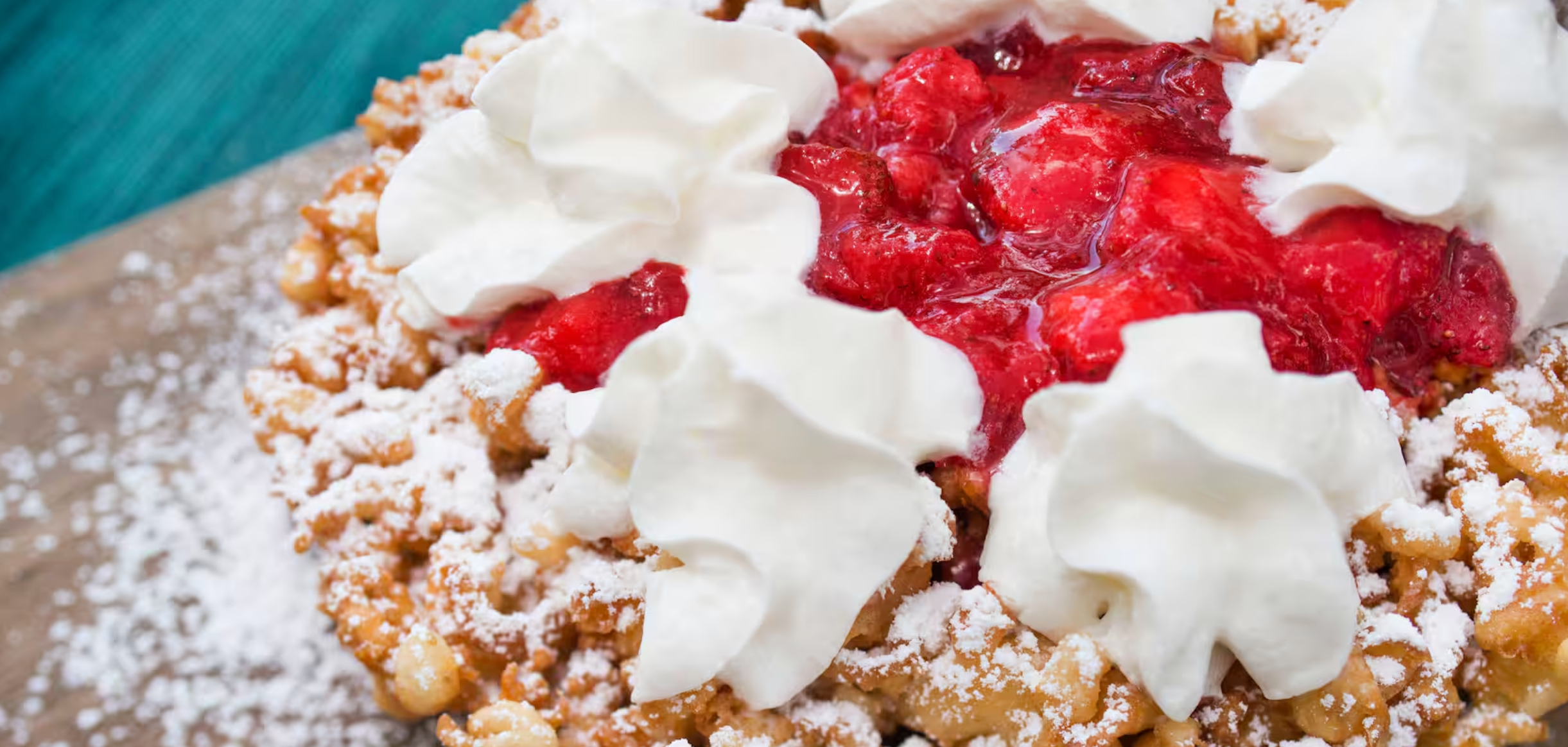 Freshly baked strawberry cobbler topped with whipped cream and buttery crumble topping on rustic wooden surface.