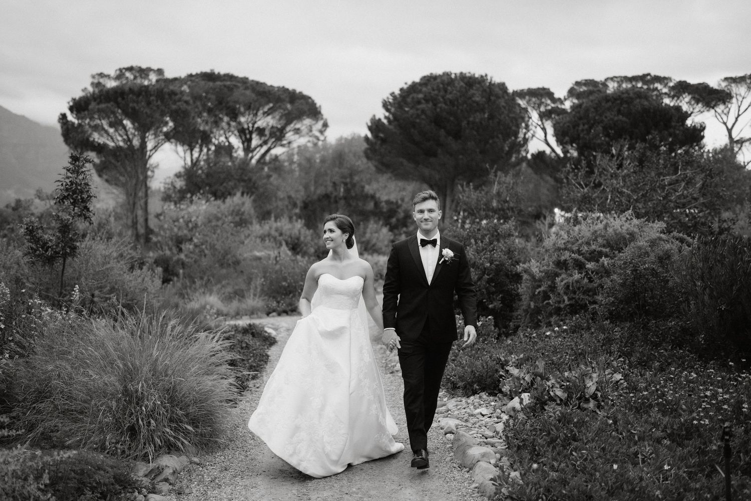 A couple walks hand in hand across a green hillside with misty mountains in the background on their wedding day.