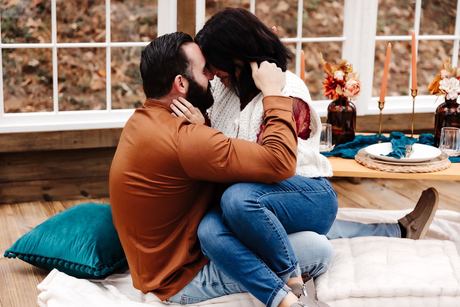 Couple sits on wooden deck with blue cushions and orange flowers during outdoor picnic together.