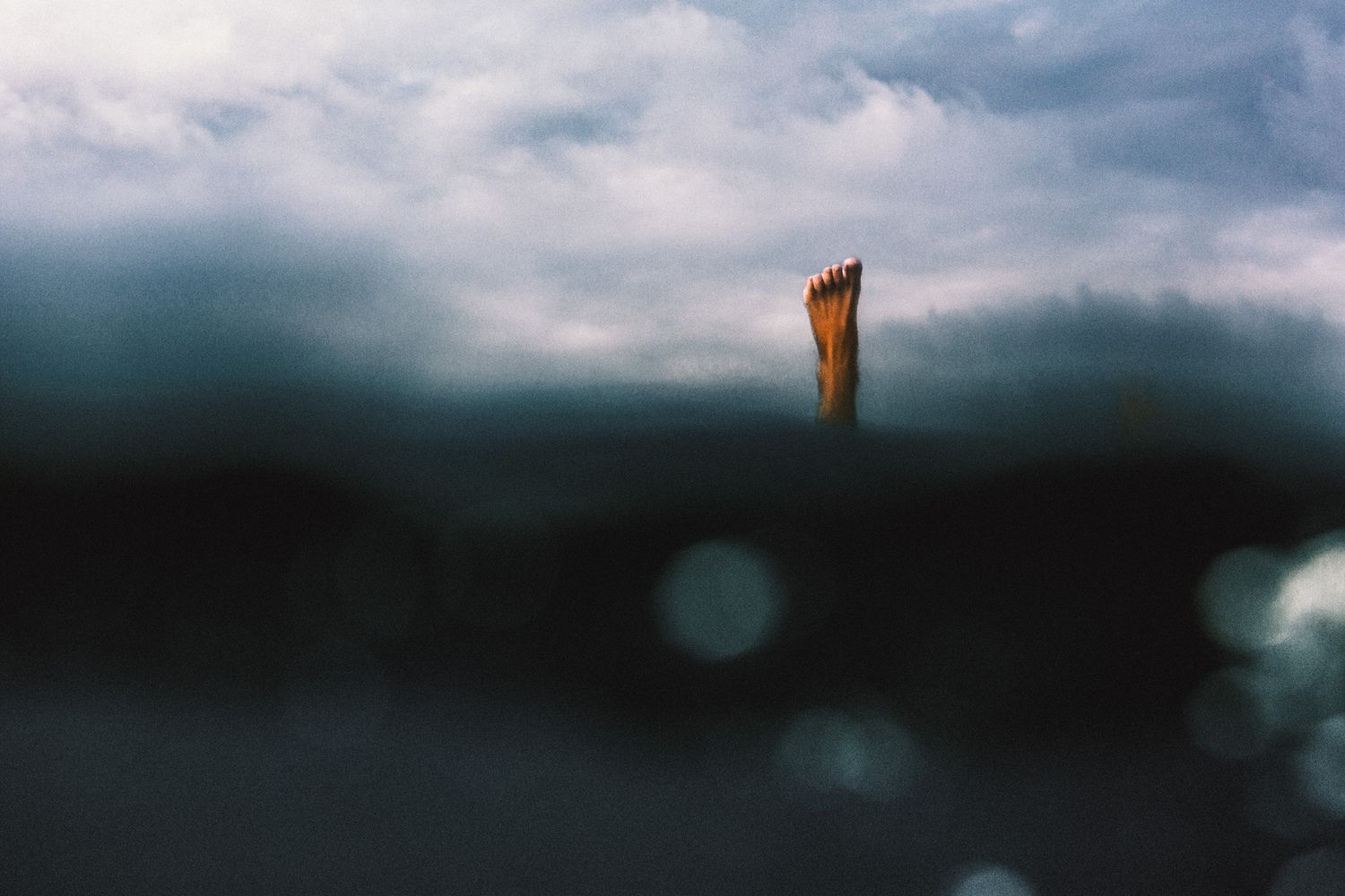 A single orange fin breaks through dark moody ocean waters under a stormy cloudy sky.