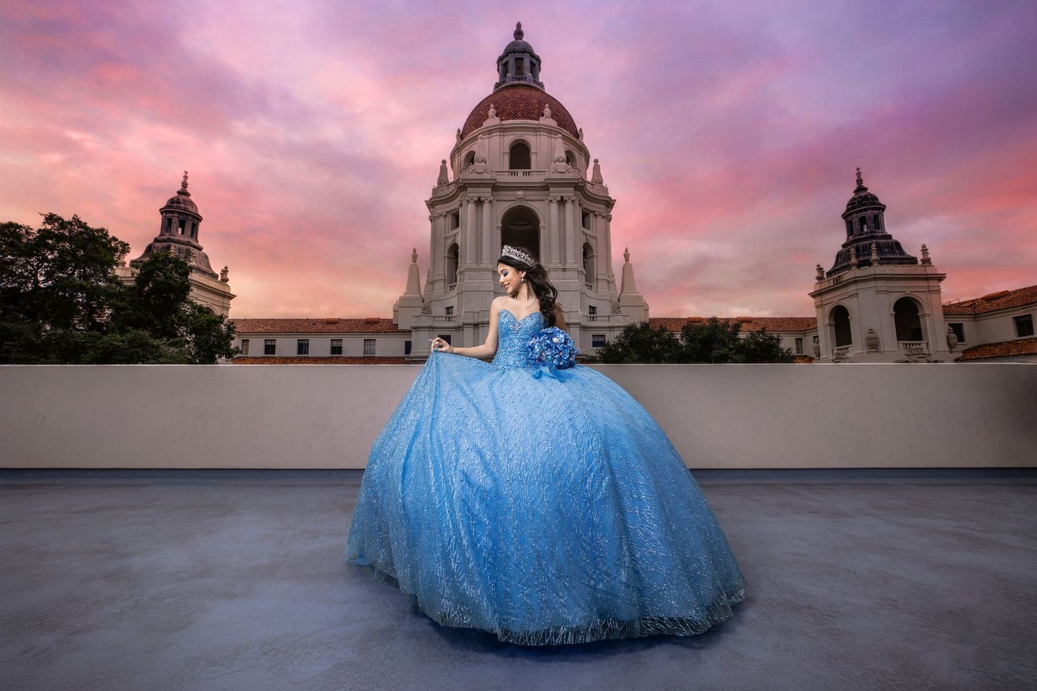 A flowing blue ball gown dress photographed in front of Pasadena City Hall during a dramatic pink sunset.