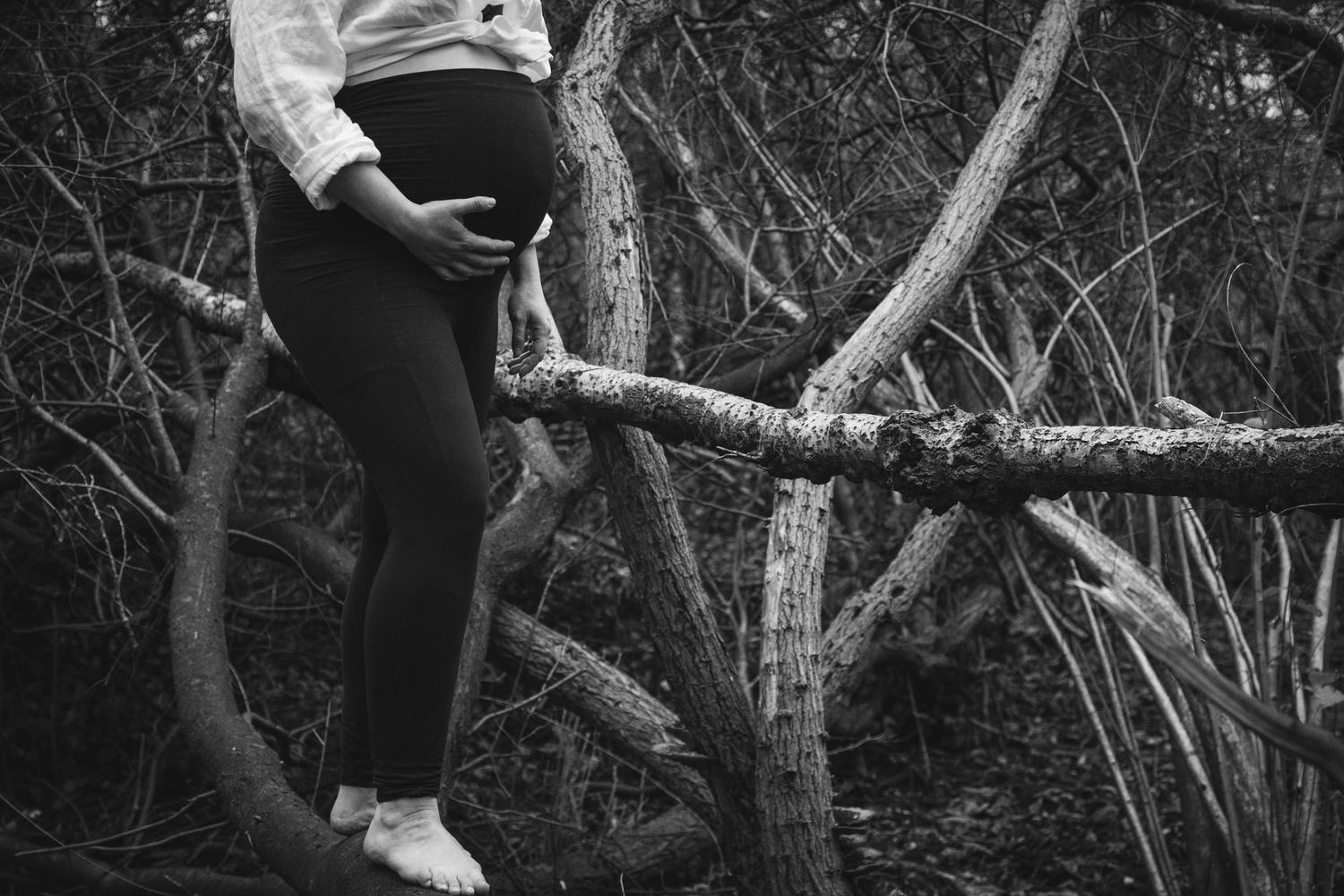 Black and white artistic photo showing bare feet on a tree branch in a moody forest setting.