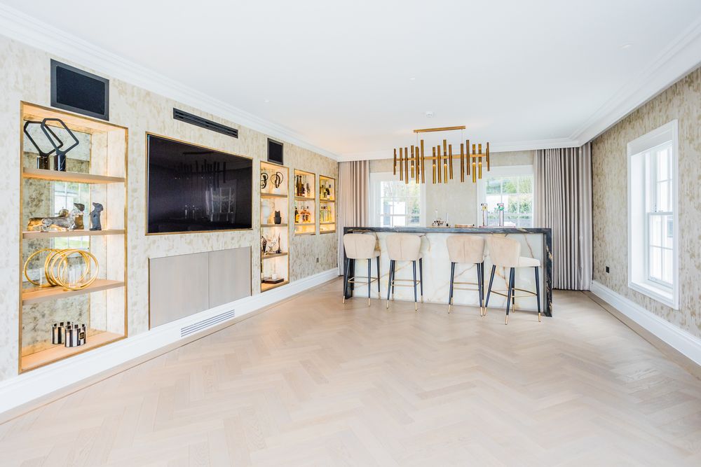 Modern luxury living room with gold chandelier, white bar stools, and built-in wall shelving.