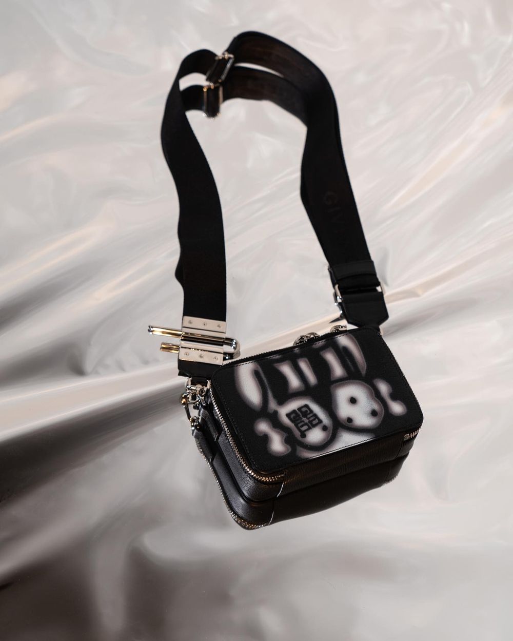 Black leather mini bag with strap hanging against white backdrop.
