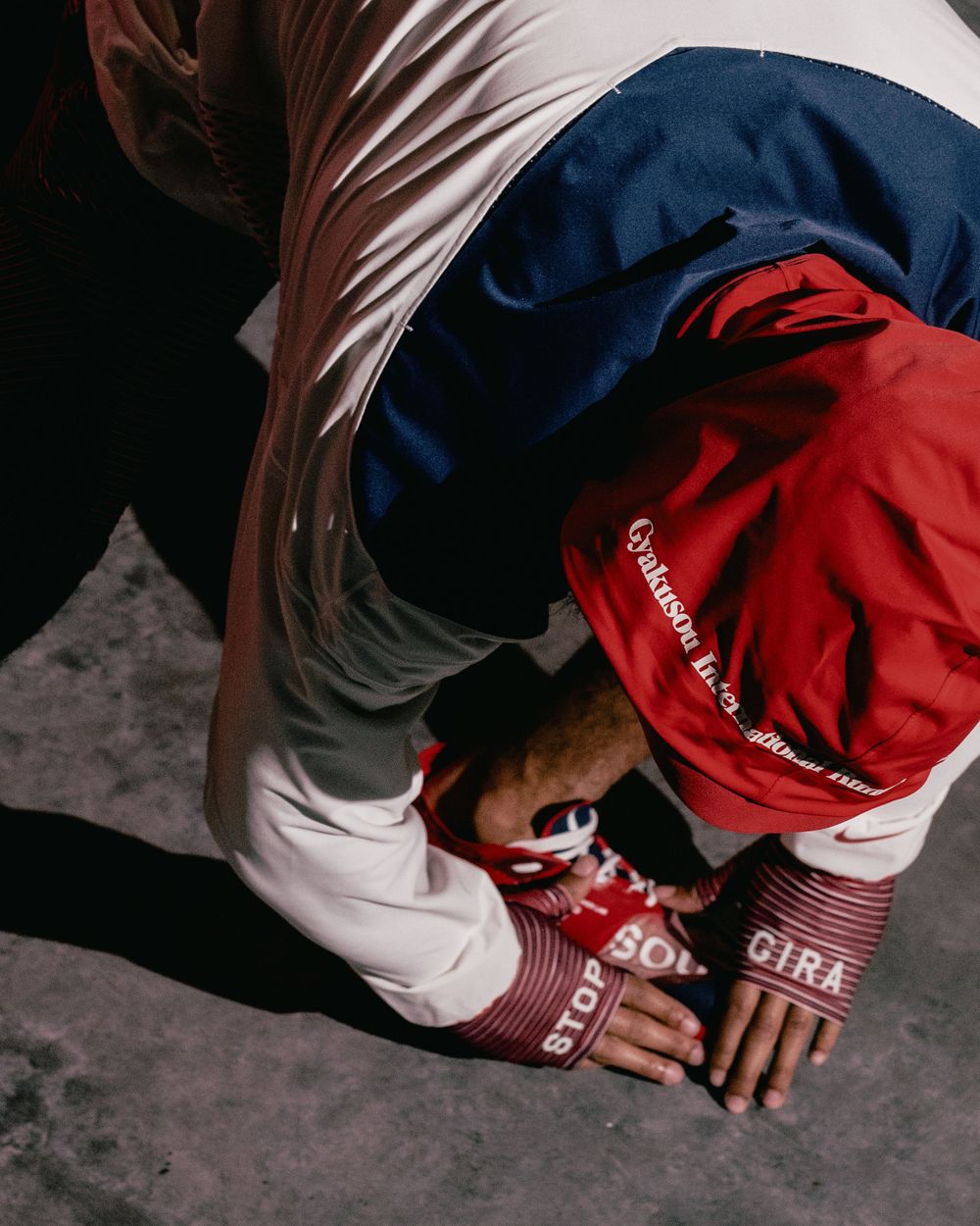 Overhead view of person in red cap and white clothing crouching on ground.