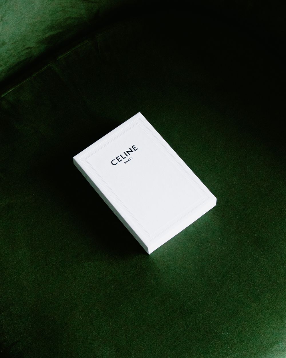 White Celine box photographed on dark green velvet surface.