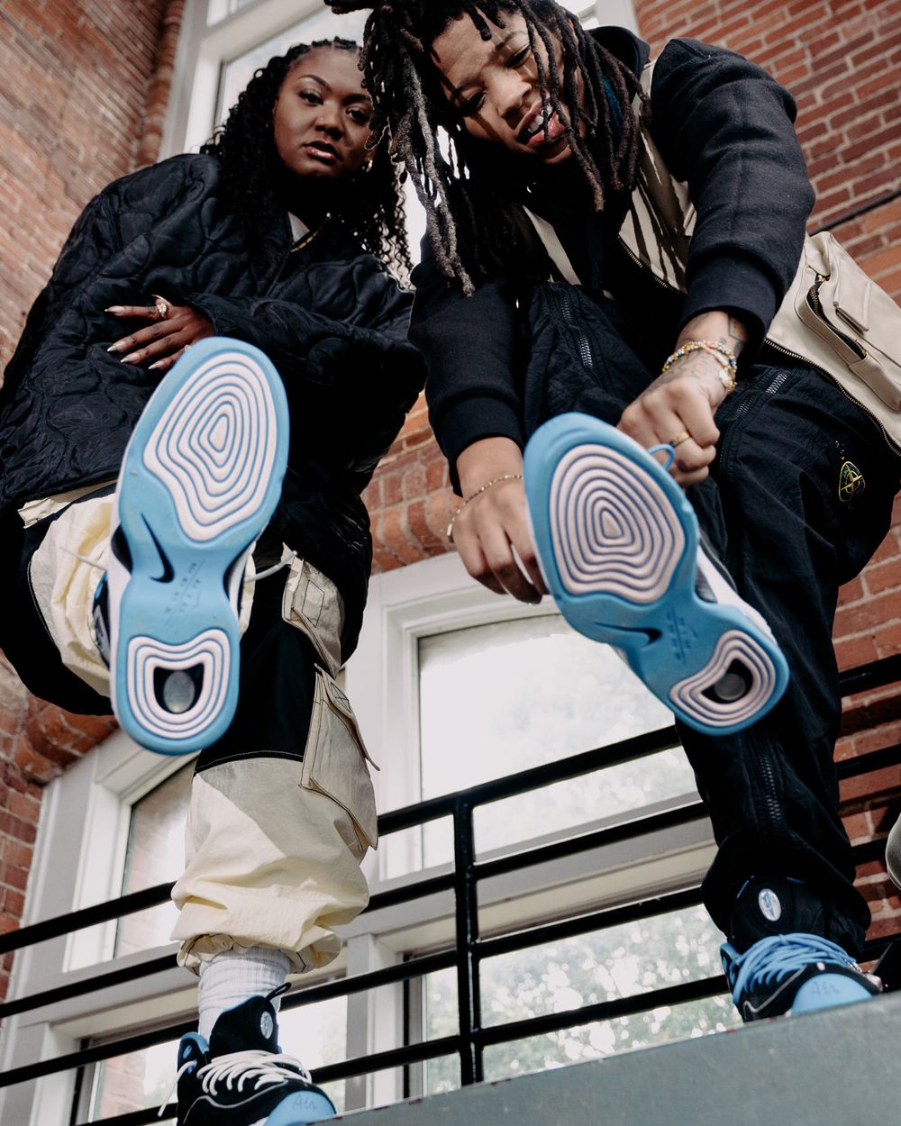 Two people showing off blue-soled sneakers while sitting on brick building steps.