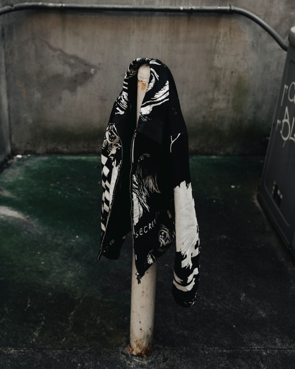 Black and white graphic print hoodie hanging on metal pole in dark industrial setting.