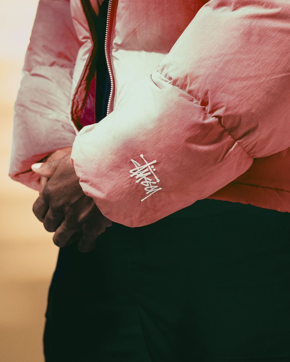 Close-up of pink Stussy jacket sleeve detail against blurred background.