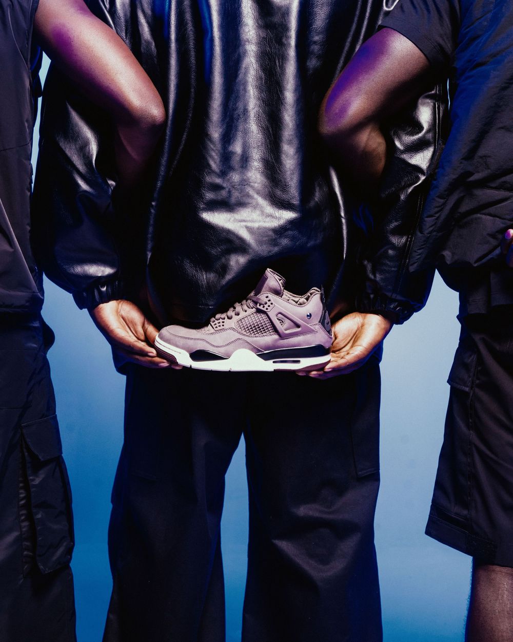 Person holding purple and gray sneakers against a blue background while wearing dark clothing.