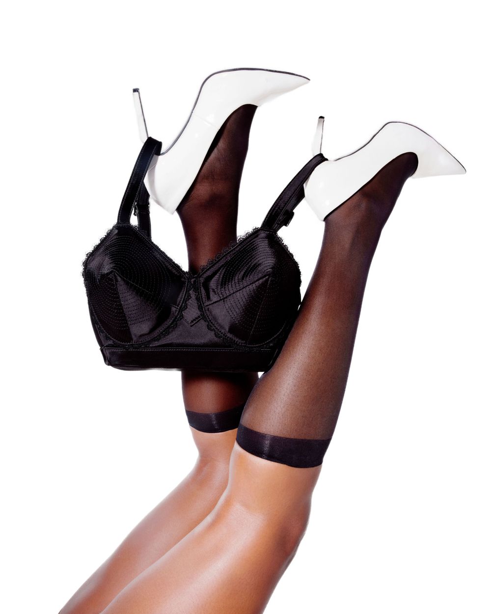 Black lingerie and white stiletto heels with sheer stockings in artistic pose.