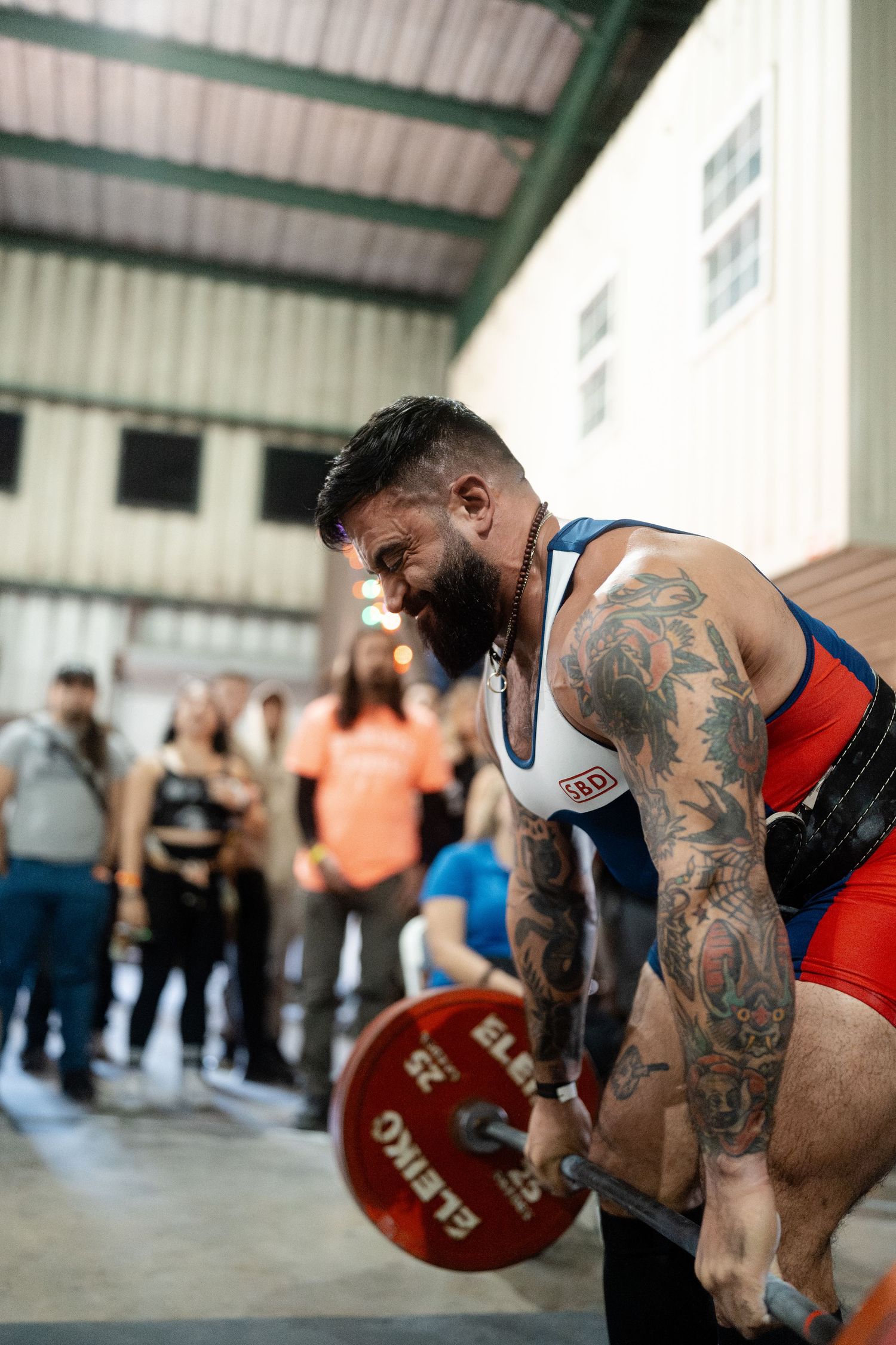 A powerlifter with tattoos prepares to lift a heavy barbell during a competition.