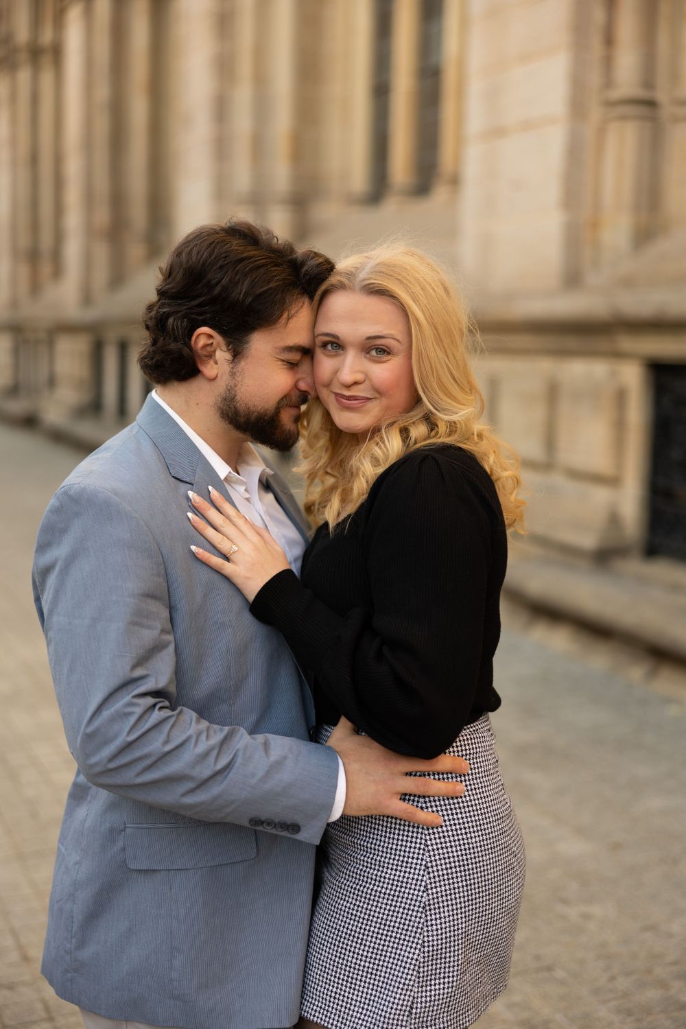 A romantic moment between a couple in formal attire posing against stone architecture.