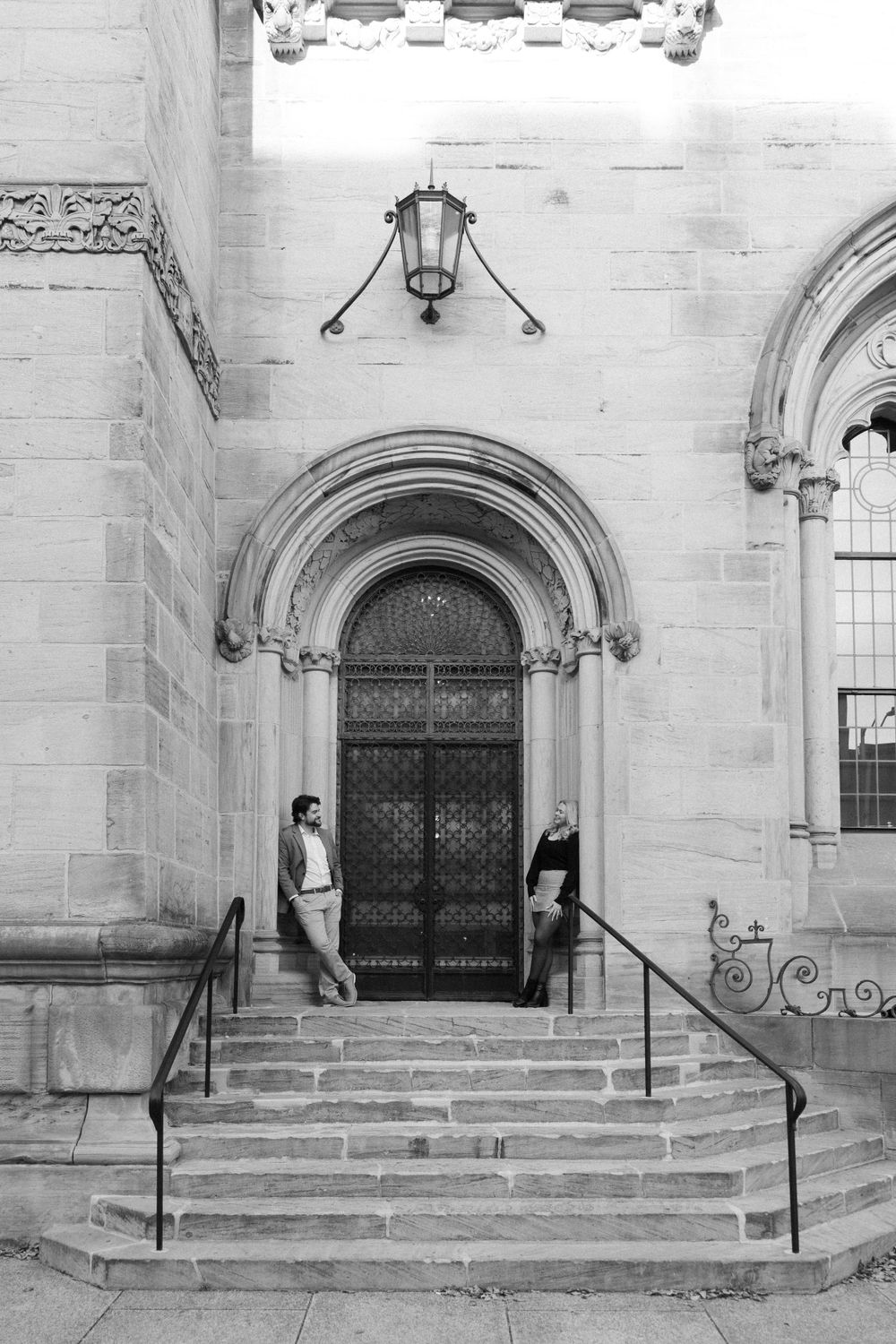 A black and white photo of two people standing on stone steps by an ornate church entrance.