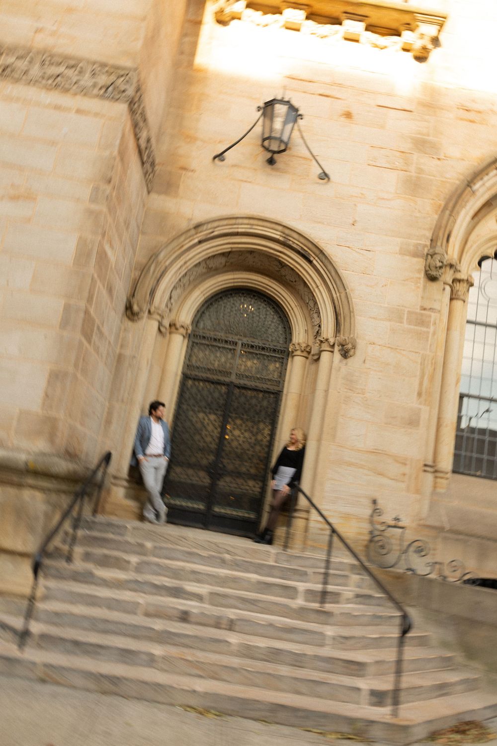 A tilted architectural photo of two people on church steps with a vintage lantern above.