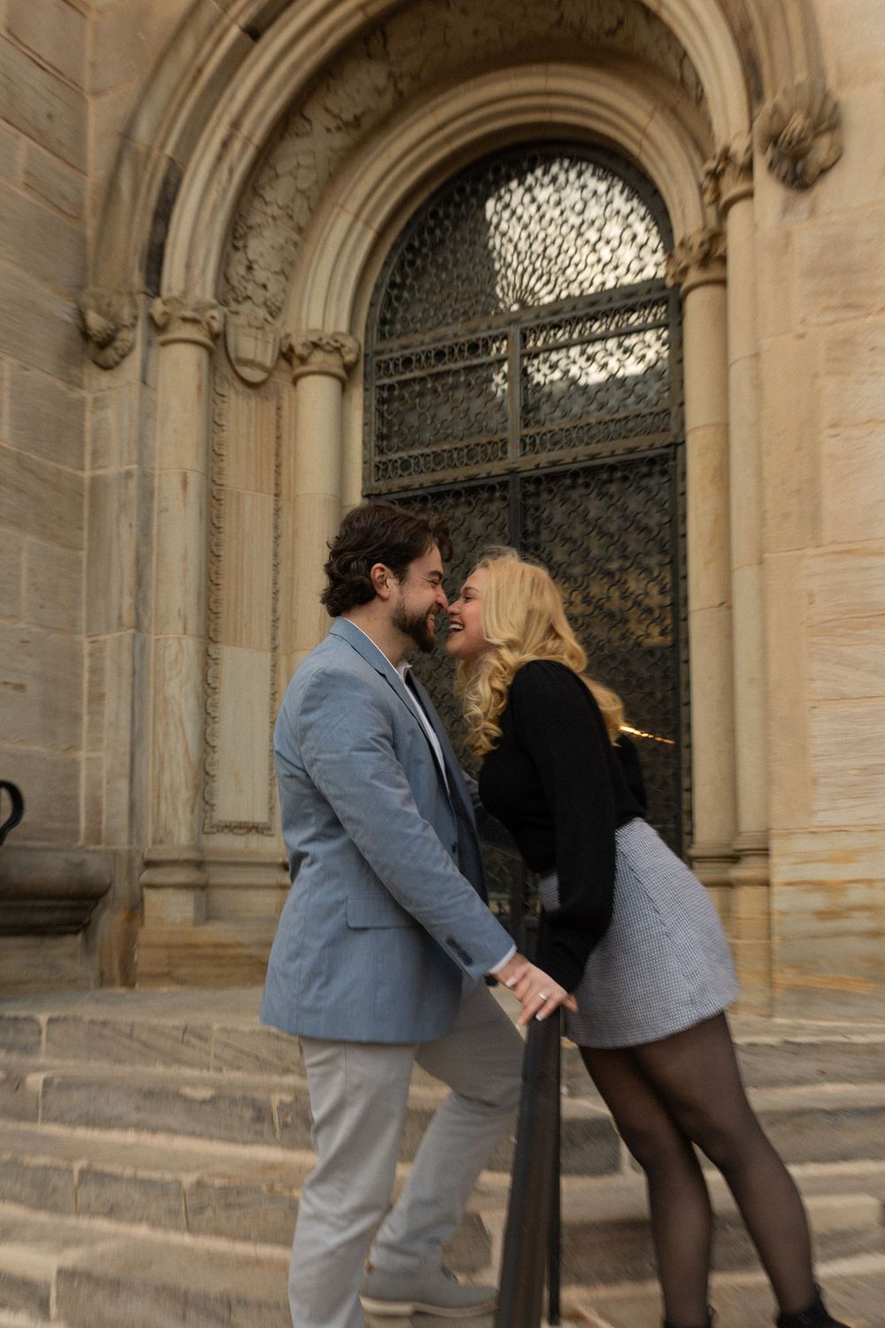 A couple shares an intimate moment on stone steps against gothic church architecture.