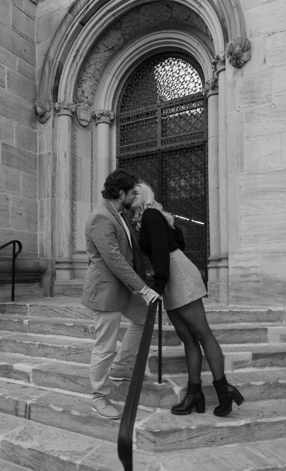 A black and white photo of a couple posing romantically on church steps.